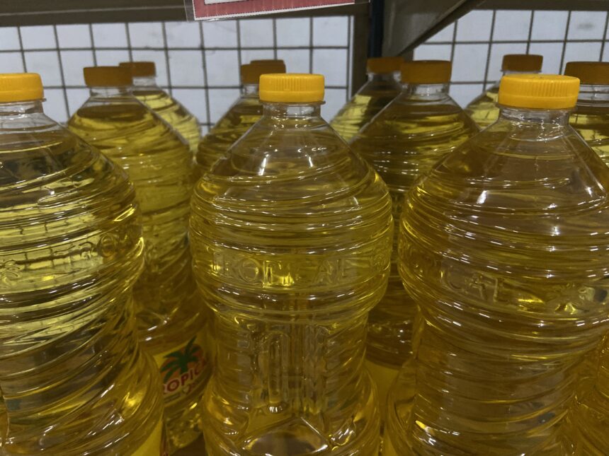 Rows of clear plastic bottles filled with yellow cooking oil on a store shelf with yellow caps