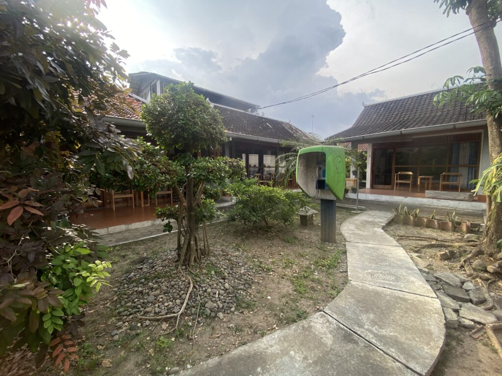 Courtyard of a tropical-style home with tiled roofs, lush plants, and a curved concrete path.