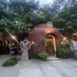 Entrance to a pottery museum with a red brick dome and a sign reading 'MuseumKugErabah Timbulharjo' amid trees and decorative lights