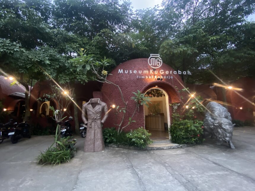 IMG_8263 - Mabur.co Entrance to a pottery museum with a red brick dome and a sign reading 'MuseumKugErabah Timbulharjo' amid trees and decorative lights