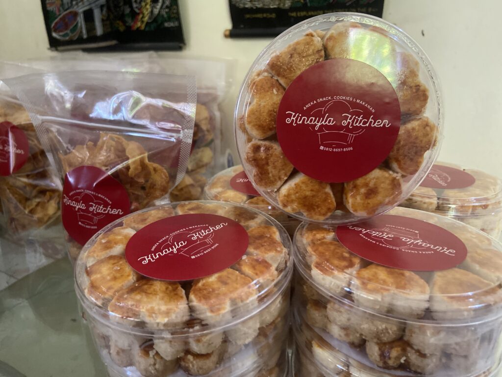 Clear plastic containers of round cookies with red Kinayla Kitchen labels on a display shelf.