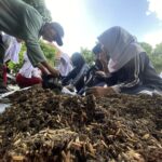 Students in uniforms kneeling around a large pile of mulch, planting outdoors with a teacher or adult guiding them.