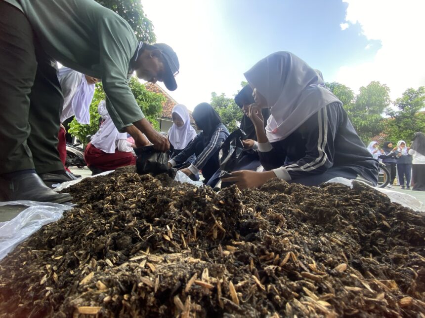 IMG_8359 - Mabur.co Students in uniforms kneeling around a large pile of mulch, planting outdoors with a teacher or adult guiding them.