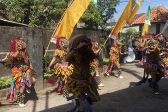 Dancers in colorful traditional costumes with masks and bell anklets perform in a street parade under yellow banners.