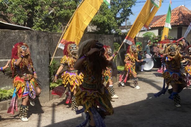 Dancers in colorful traditional costumes with masks and bell anklets perform in a street parade under yellow banners.