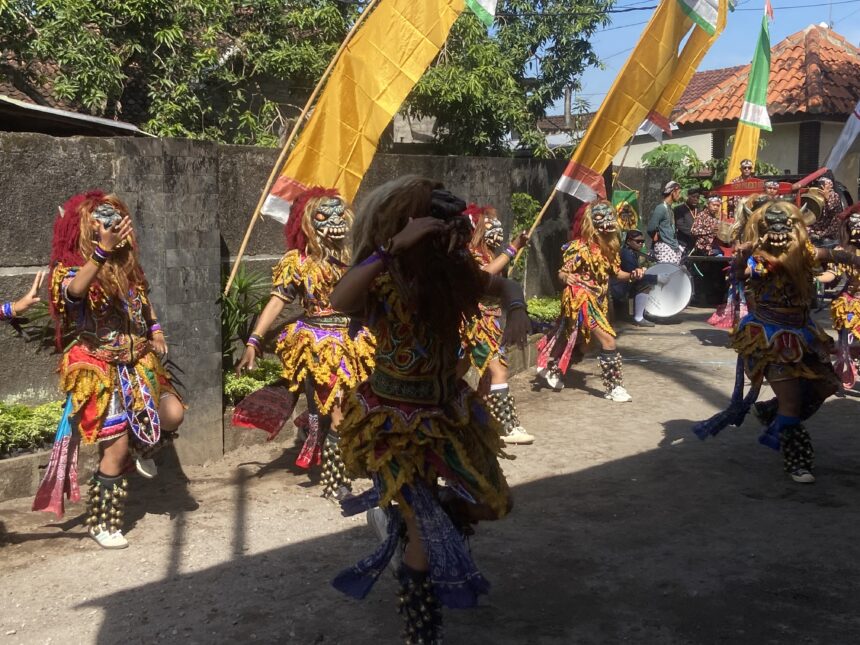 Dancers in colorful traditional costumes with masks and bell anklets perform in a street parade under yellow banners.