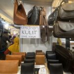 Shelf of leather bags in brown and black at a market stall, with a handwritten sign reading 'Kerajinan Kulit Khas Yogya' in the background.