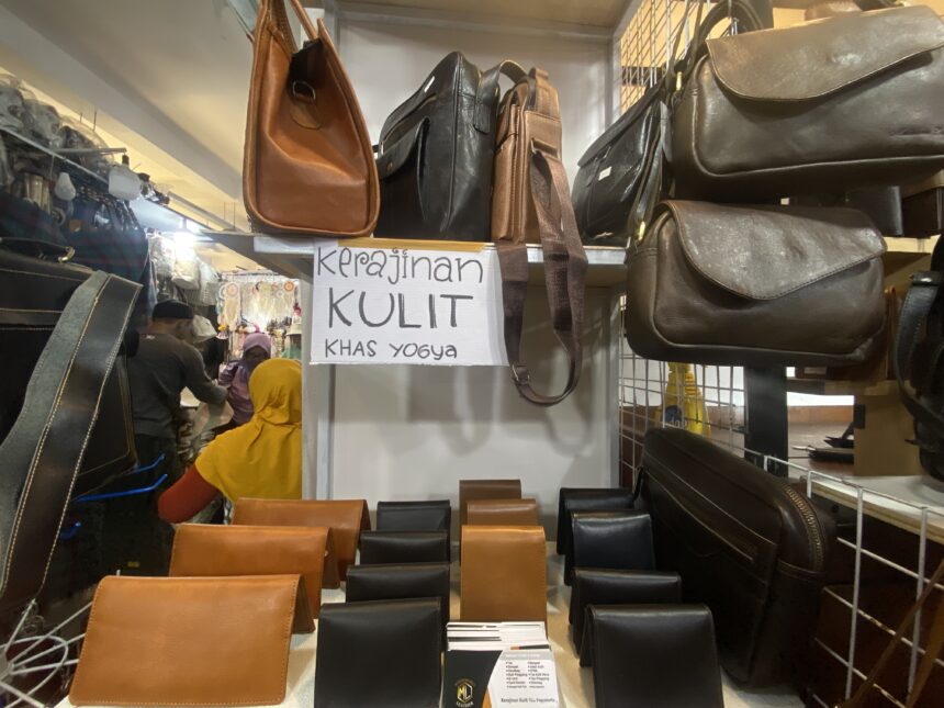 IMG_8582 - Mabur.co Shelf of leather bags in brown and black at a market stall, with a handwritten sign reading 'Kerajinan Kulit Khas Yogya' in the background.