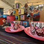 Colorful hand-painted mugs stacked on a market stall, featuring floral designs and bold colors.