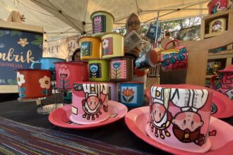 Colorful hand-painted mugs stacked on a market stall, featuring floral designs and bold colors.
