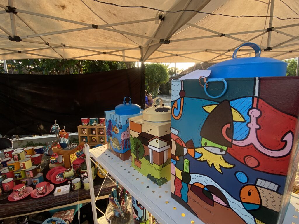 Colorful market stall with a large cartoon mural on the wall, and shelves of colorful cups, plates, and kitchenware under a beige canopy.