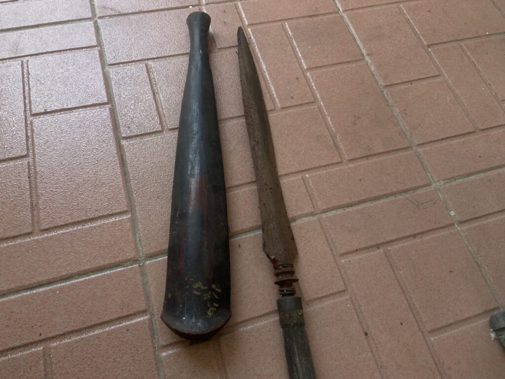 Two long, worn tool-like objects with handles lying on a brick-paved surface; one is black and tapering, the other is rusted brown and broken near the grip.