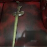 Antique curved dagger with ornate handle lying on a red leather sofa.