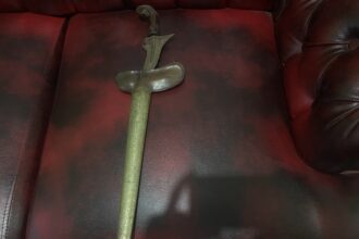 Antique curved dagger with ornate handle lying on a red leather sofa.