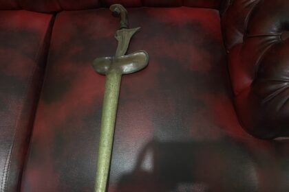 Antique curved dagger with ornate handle lying on a red leather sofa.