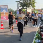 Runners participate in a road race while spectators cheer from the sidewalk on a sunny day.