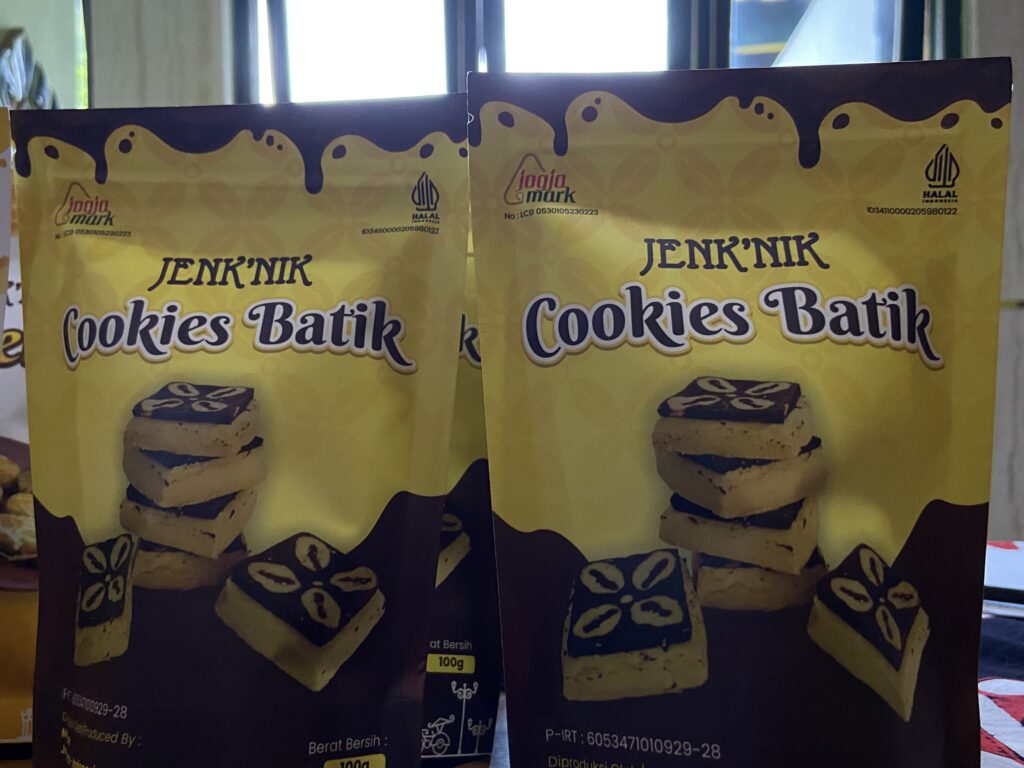 Two yellow cookie packaging boxes labeled 'JENK'NIK Cookies Batik' with blue-brown designs and a chocolate cube image, set side by side in a display.