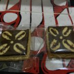 Two rectangular marble cake slices in clear plastic wrappers on a red patterned surface, showing light and dark swirled batter.