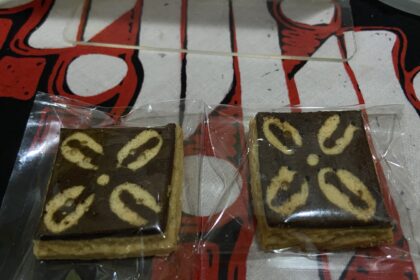 Two rectangular marble cake slices in clear plastic wrappers on a red patterned surface, showing light and dark swirled batter.