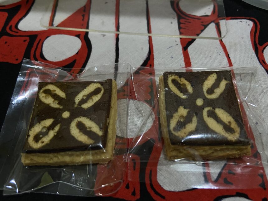 Two rectangular marble cake slices in clear plastic wrappers on a red patterned surface, showing light and dark swirled batter.