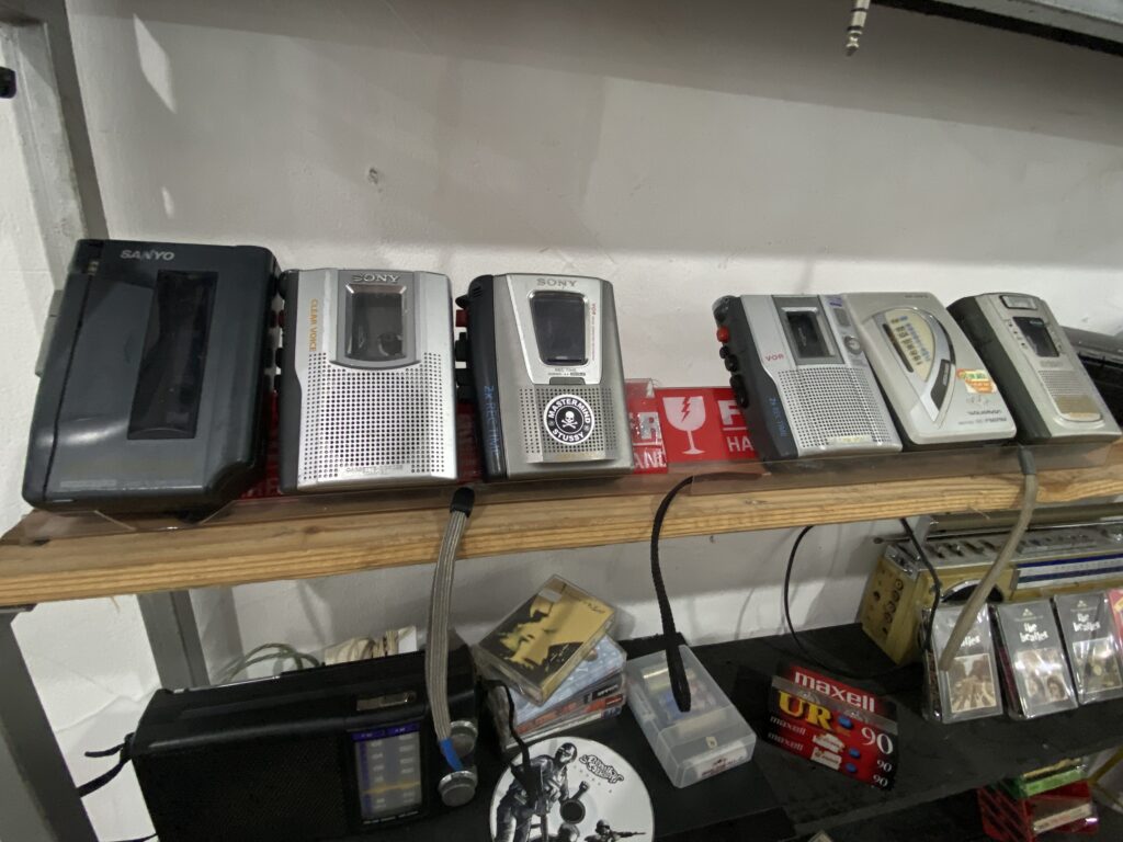 Row of vintage portable radios and cassette players lined up on a display shelf in a store.
