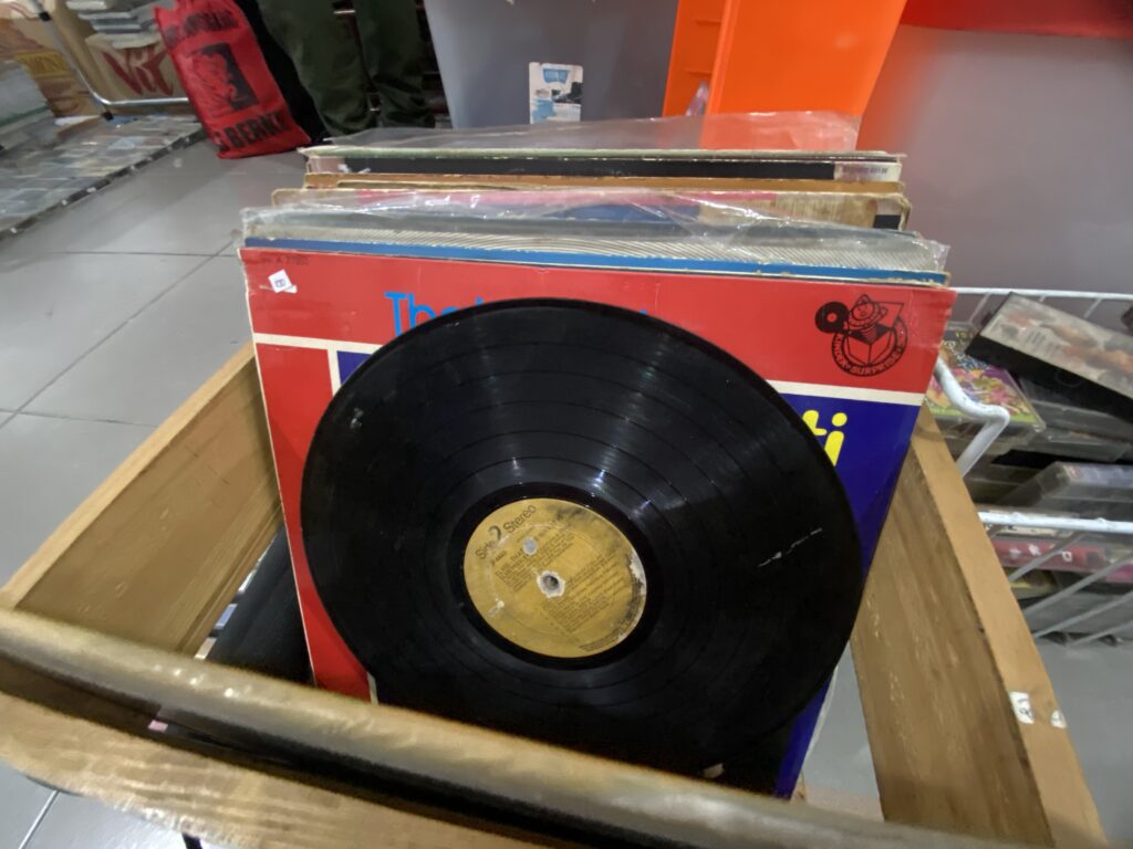 Stack of vinyl records in a display rack, with a large black LP at the front in a shop window/standuee context.