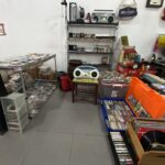 Cluttered room with shelves holding old electronics, cassette tapes, and CDs scattered on tables and shelves.