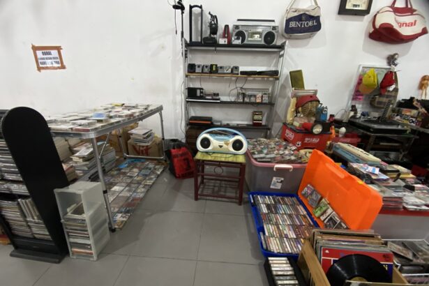 Cluttered room with shelves holding old electronics, cassette tapes, and CDs scattered on tables and shelves.