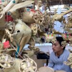 Young man inside a market stall surrounded by intricate woven palm leaf decorations.