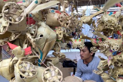 Young man inside a market stall surrounded by intricate woven palm leaf decorations.