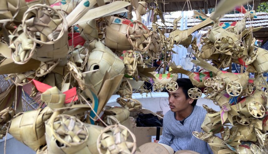 Young man inside a market stall surrounded by intricate woven palm leaf decorations.