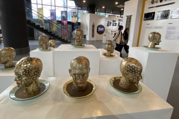 Group of gold-polished bust sculptures with white polka dots arranged on white pedestals in a modern museum gallery, with visitors in the background.”