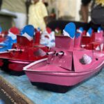 Close-up of colorful miniature pink and red toy boats with blue sails on a blue wooden surface