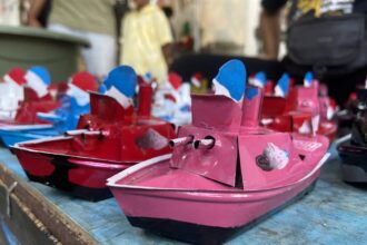 Close-up of colorful miniature pink and red toy boats with blue sails on a blue wooden surface