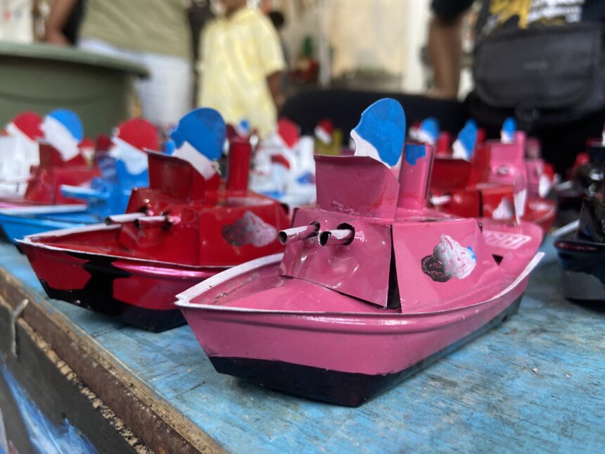 Close-up of colorful miniature pink and red toy boats with blue sails on a blue wooden surface