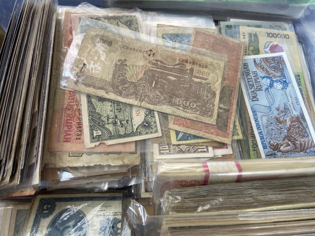 Pile of old banknotes in plastic sleeves in a box, various currencies and denominations visible.