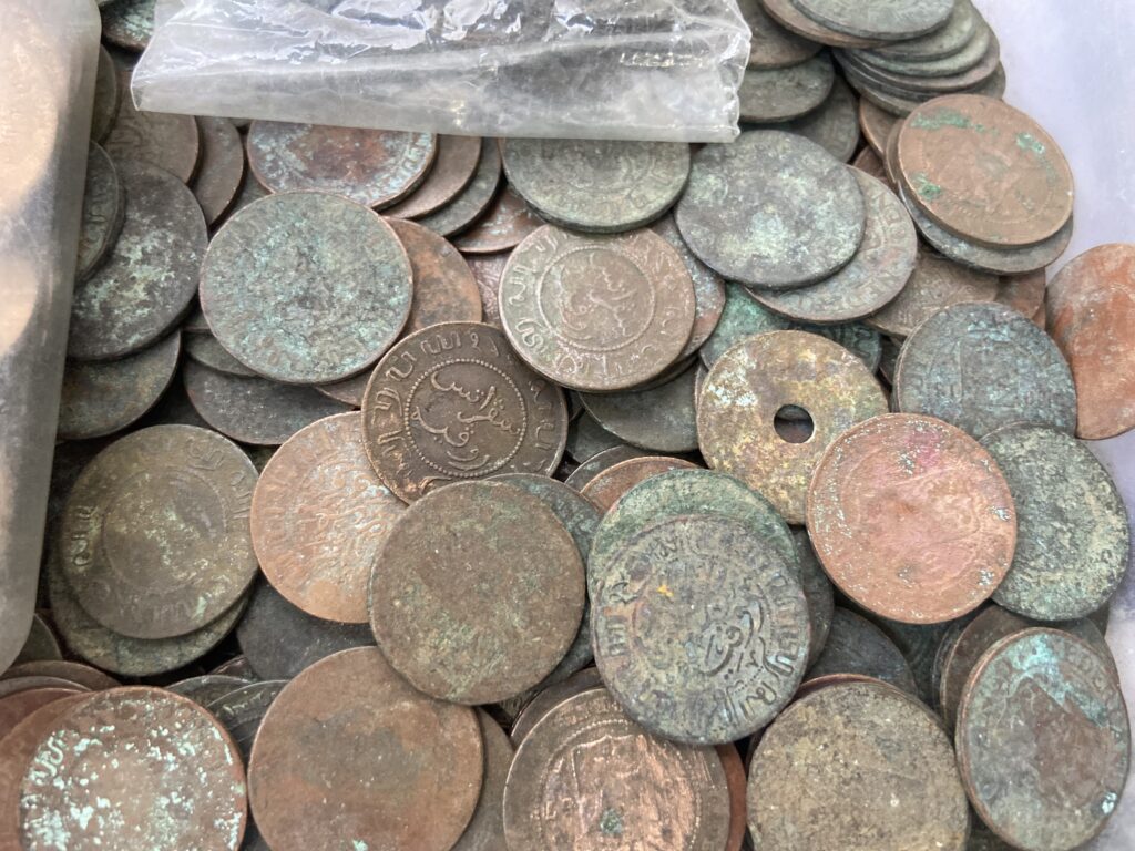Pile of old copper coins with green patina scattered in a container.