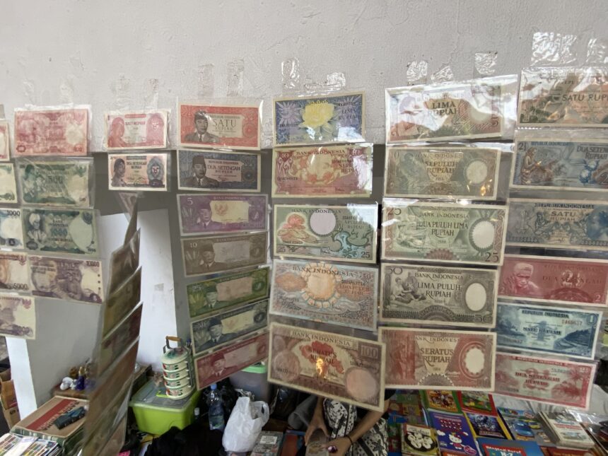 Display of Indonesian banknotes in plastic sleeves arranged on shelves, showing multiple colorful denominations of Rupiah.