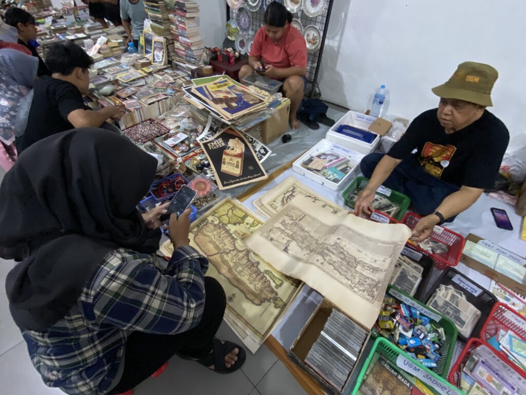 People browse a busy stall filled with books, posters, and maps laid out on tables and shelves