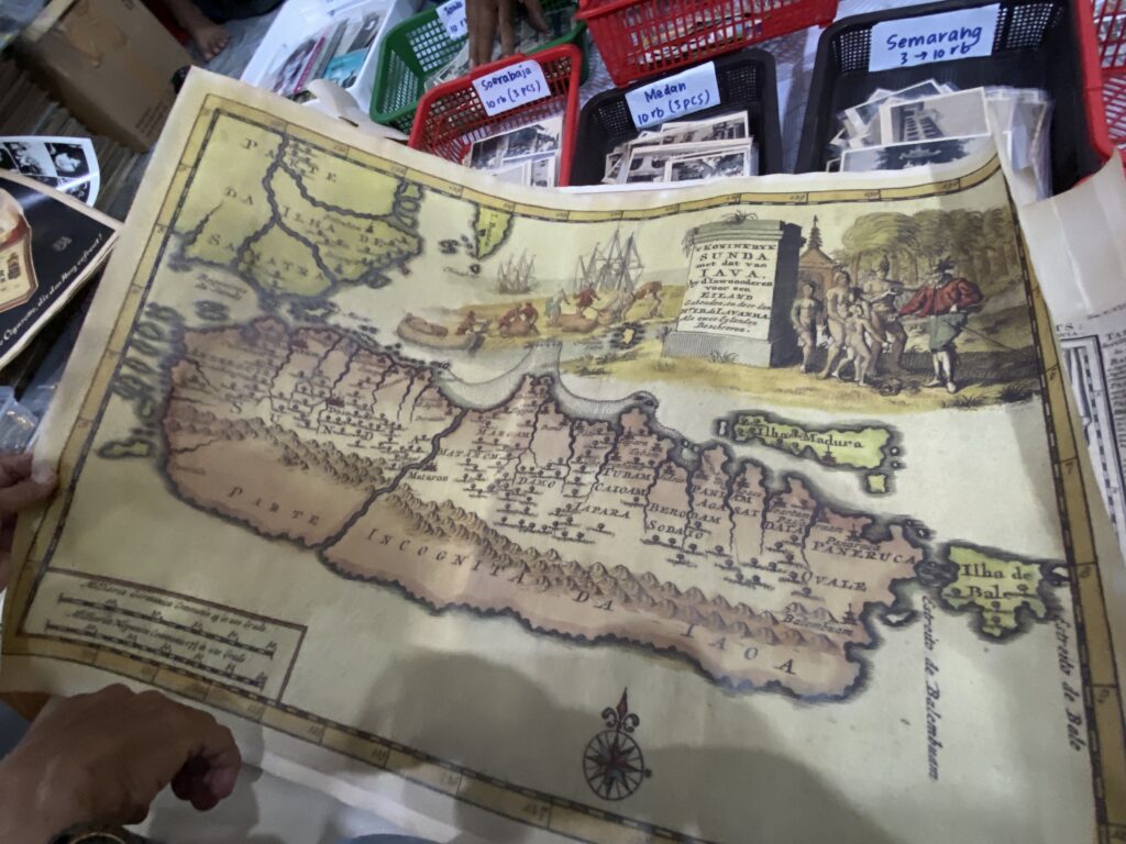 Antique illustrated map spread on a table, showing coastlines, ships, and a compass rose at a market stall.