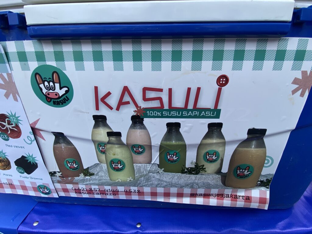 IMG_9344 - Mabur.co Bottles of milk drinks with a green circular cow logo, lined up on a display with a checkered green design and sign in the background.
