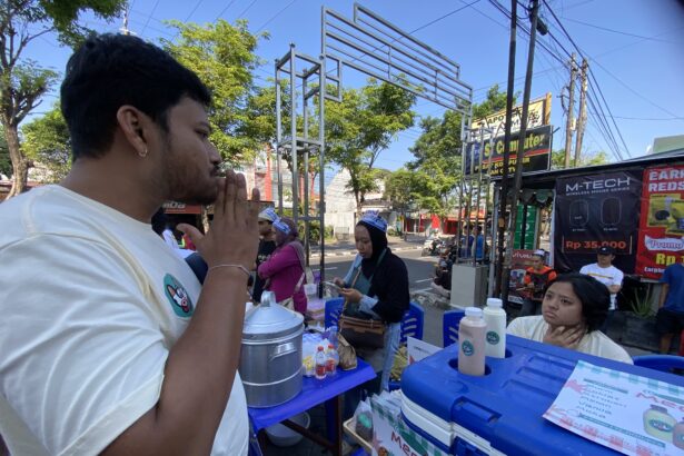 Side-profile of a man in a light shirt at an outdoor street market, standing by a vendor table with blue coolers and menus visible in the foreground