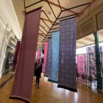 Indoor hallway with colorful patterned fabric banners suspended from a metal framework ceiling.