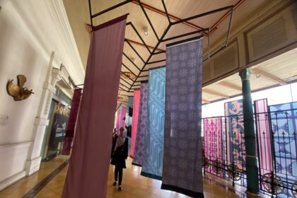 Indoor hallway with colorful patterned fabric banners suspended from a metal framework ceiling.