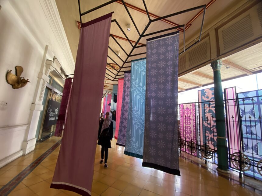 Indoor hallway with colorful patterned fabric banners suspended from a metal framework ceiling.