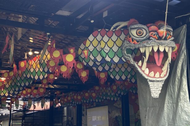 Dragon head sculpture with sharp teeth and orange eye, indoors among colorful hanging banners and lantern-like decorations.
