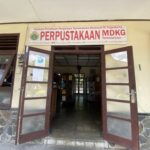 Open double doors to a library entrance with a large sign reading 'PERPUSTAKAAN MDKG Tamansiswa' above the doorway.