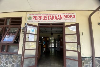 Open double doors to a library entrance with a large sign reading 'PERPUSTAKAAN MDKG Tamansiswa' above the doorway.