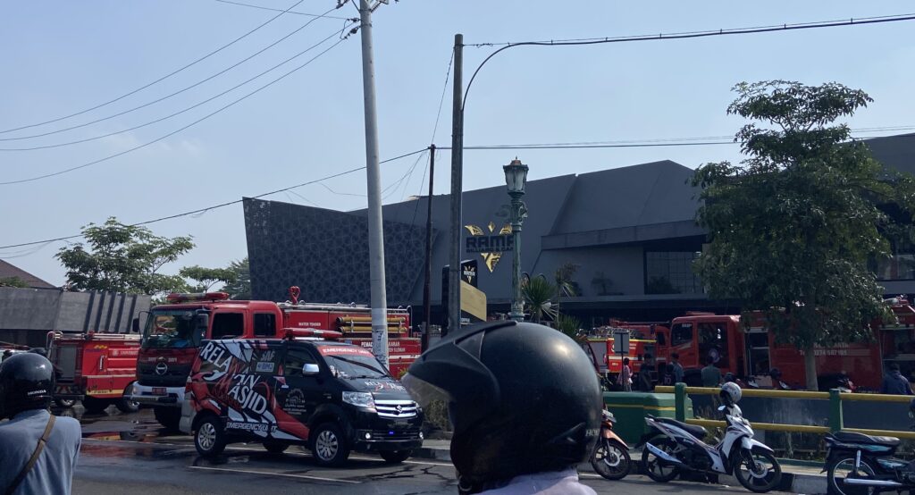 Fire trucks and emergency vehicles parked along a city street with people and helmets in the foreground during an emergency response.