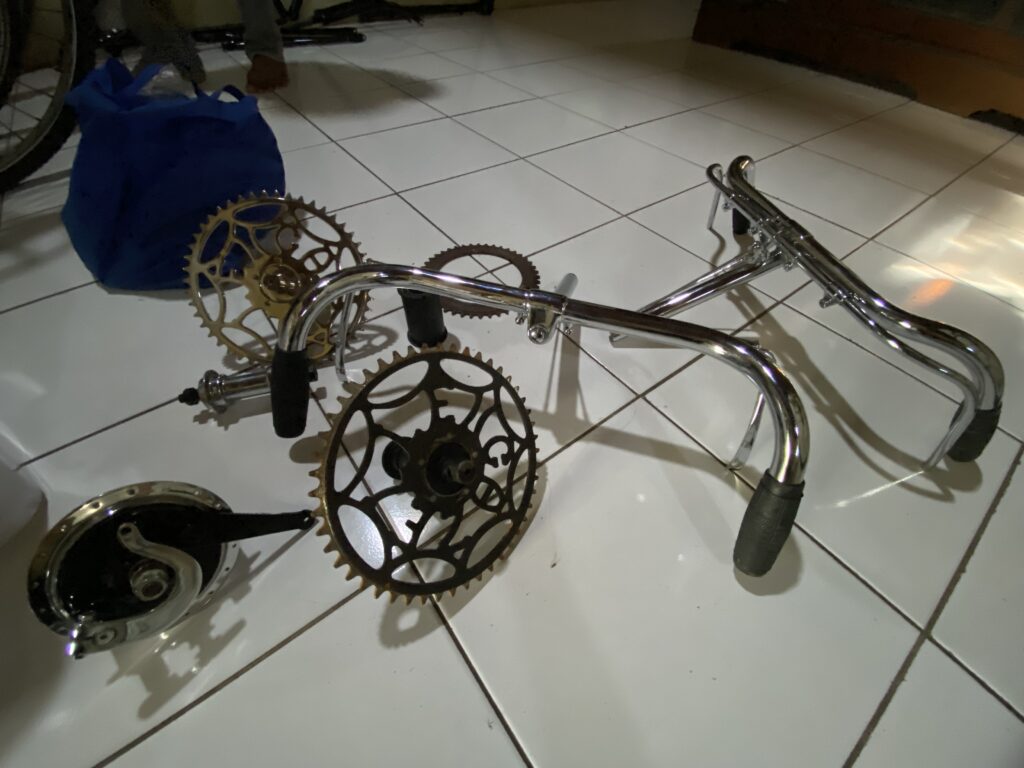 IMG_9832 - Mabur.co Disassembled bicycle on a tiled floor with large brass chainrings and a chrome frame fitness background blue bag nearby